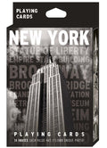 New York Black & White Playing Card Pack: The image shows the packaging for a high‑contrast black‑and‑white deck. The front displays a bold photograph of the Empire State Building with “NEW YORK” in large white capital letters at the top and faint grey landmark names beneath. “Playing Cards” appears in white at both the top and bottom. The side panels feature additional black‑and‑white images of iconic New York buildings.