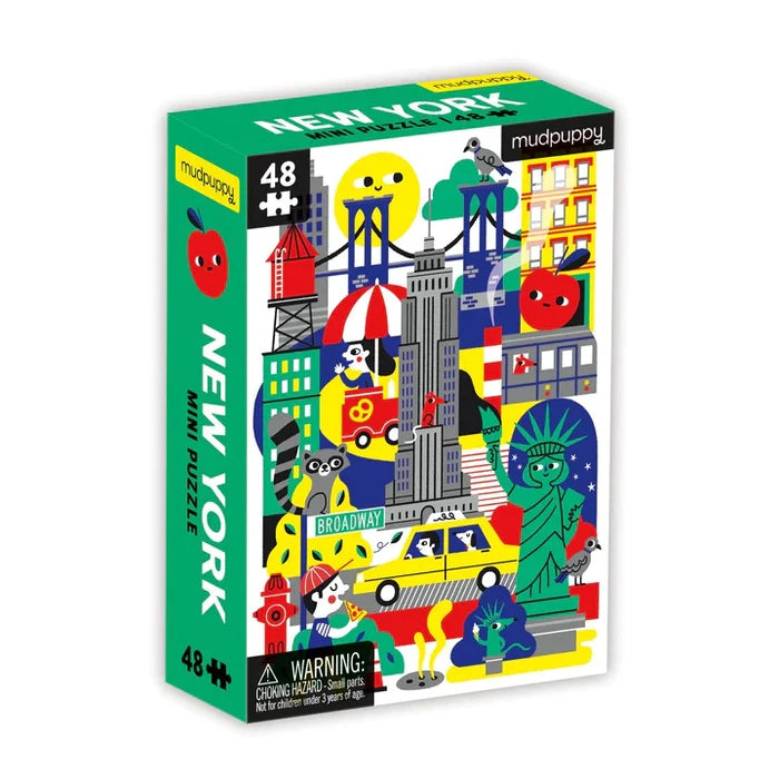 Product title: New York City Mini Puzzle 
A small, brightly colored puzzle box shows playful illustrations of New York City icons, including a water tower, the Empire State Building, the Statue of Liberty, a yellow taxi, and other classic city sights. The view is at an angle depicting the spine and cover.