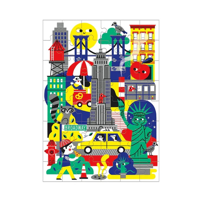 Product title: New York City Mini Puzzle 
A small, brightly colored puzzle box shows playful illustrations of New York City icons, including a water tower, the Empire State Building, the Statue of Liberty, a yellow taxi, and other classic city sights. The packaging is shown flat, displaying the full puzzle artwork on the front.