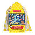 A bright yellow, house-shaped die-cut puzzle box titled “Mudpuppy: New York City” featuring high-contrast illustrations of the Statue of Liberty, Brooklyn Bridge, and a striped hot dog stand. A yellow handle at the roof peak allows a drawstring bag to flow down the sides, with product details printed along the bottom left and right edges.