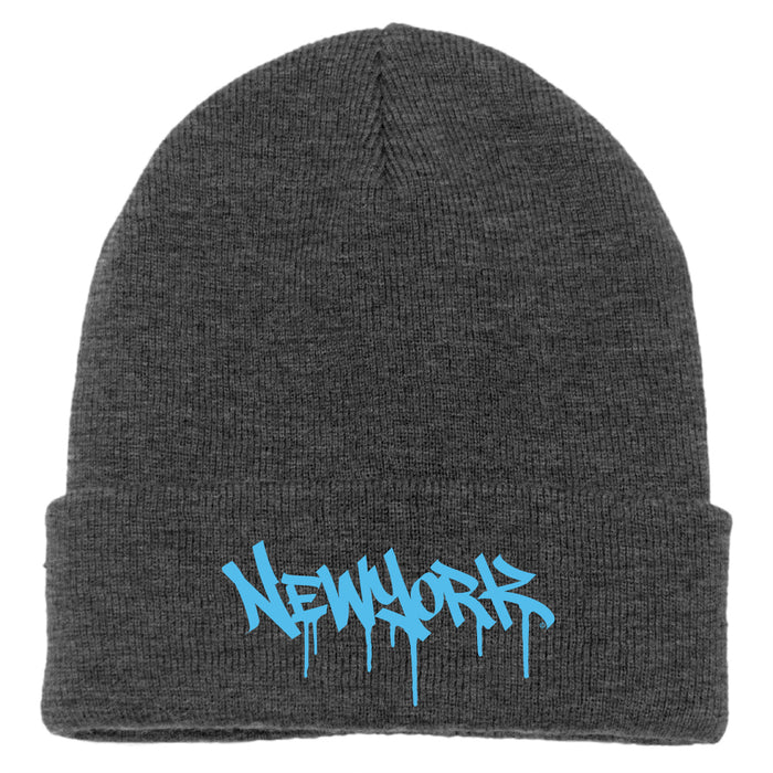 The image features a gray acrylic knit cap with a folded cuff, accented by aquamarine blue melting block-letter text spelling “New York.”