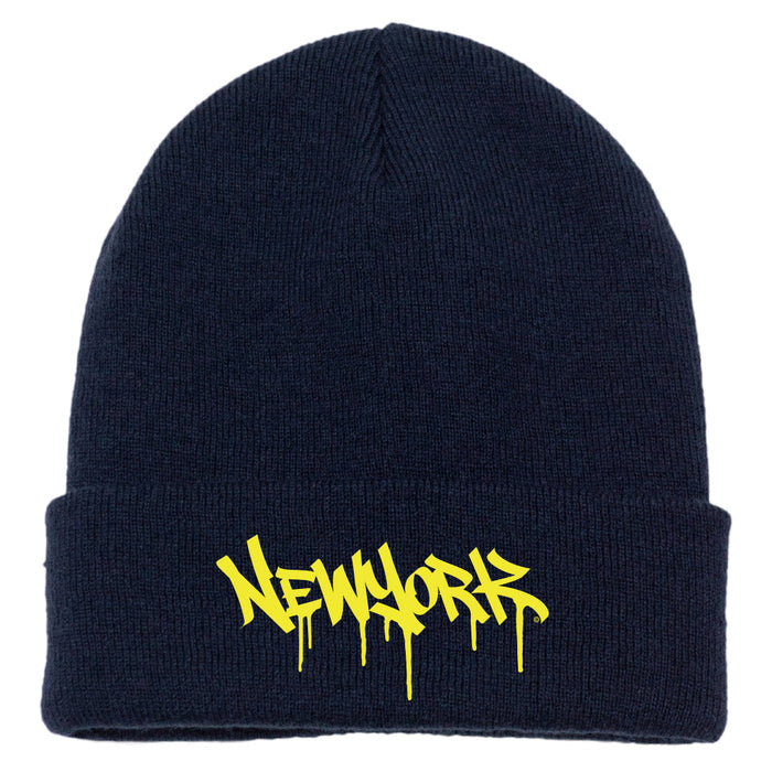 The image features a navy acrylic knit cap with a folded cuff, accented by bright yellow melting block-letter text spelling “New York.”