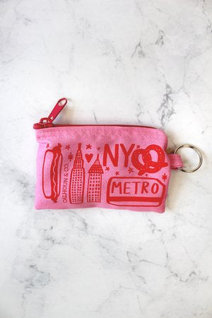 New York Screen Printed Coin Pouch, pink background with orange line drawing: A small, soft fabric pouch with a smooth, flat surface and a zipper along the top edge. The pouch is rectangular and lightweight, easy to hold in one hand. The front is printed with bold, high‑contrast New York–themed graphics—clean shapes and simple lettering—with no raised textures. The fabric feels flexible but sturdy, designed to hold coins or small items securely.