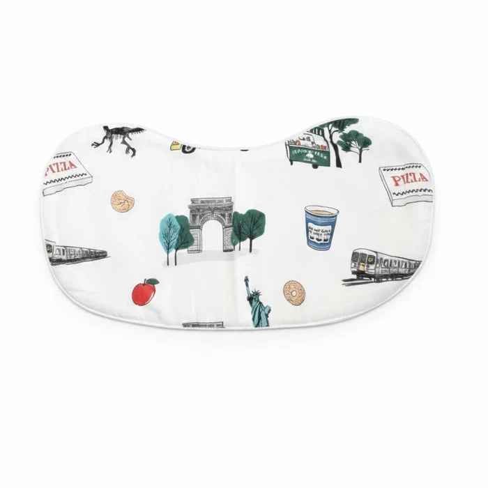 The image shows the NYC Burp Cloth and Bib Combo displayed open against a white background. The white fabric is patterned with colorful illustrations of New York City landmarks and favorites, including a blue Greek coffee cup, a black-and-white subway car, a pizza box, a sesame bagel, a green food cart, the Washington Square Arch framed by trees, and the Statue of Liberty. The playful design celebrates familiar sights and symbols of New York City.