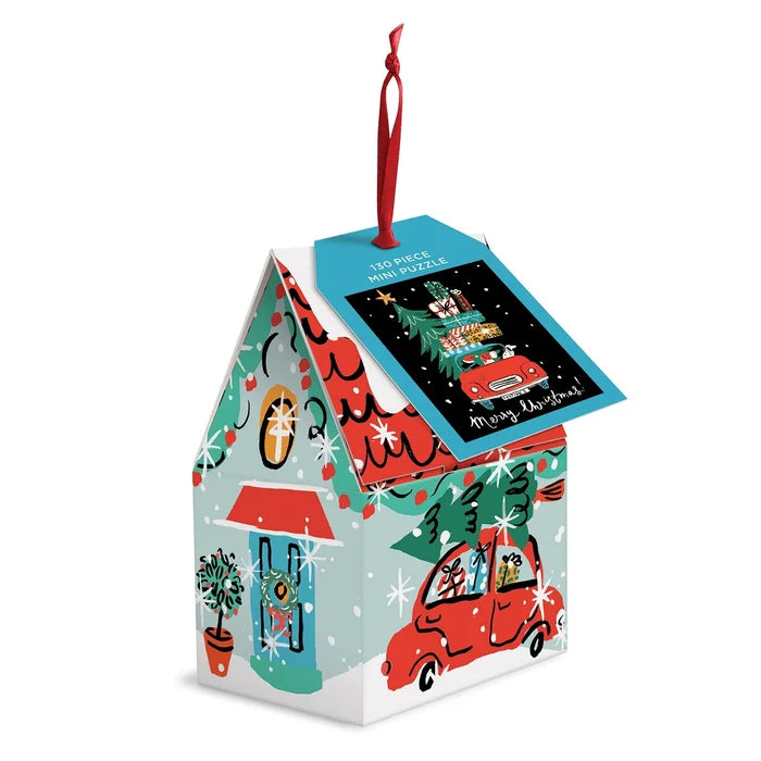 A small, house‑shaped cardboard Christmas ornament in festive red, green, blue, and white colors. The illustration shows a cheerful car packed with wrapped gifts inside a cozy holiday house. A colorful tag hangs from one side of the roof reading “130 Piece Mini Puzzle” at the top, with the gift‑filled car pictured in the middle and the words “Merry Christmas” at the bottom.