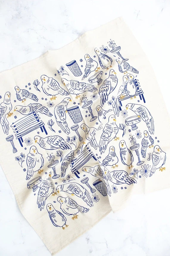 Park Pigeon Pals Screen Printed Tea Towel: This tea towel features a repeating blue and yellow line‑drawing pattern on a white background, filled with small pigeon characters in charming park scenes—perched on a bench, splashing in a puddle, and wandering by a trash can.