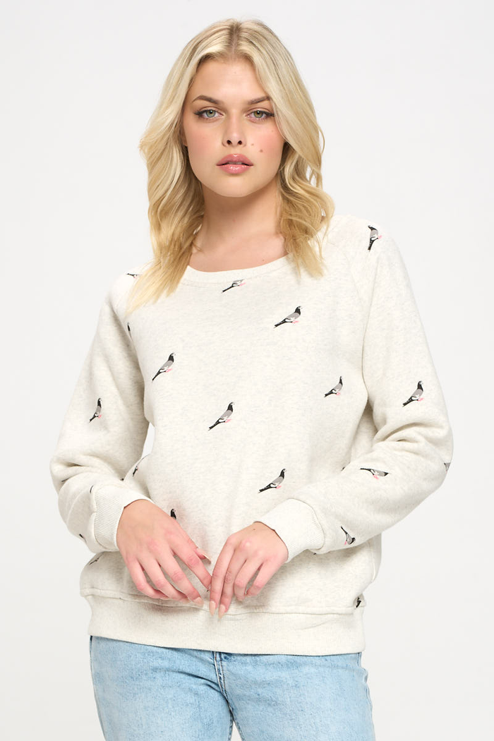 Image shows a woman wearing a crew neck heather gray sweatshirt with a pigeon print evenly repeated across the front, sleeves, and back, forming a continuous all‑over pattern rather than a single central graphic.