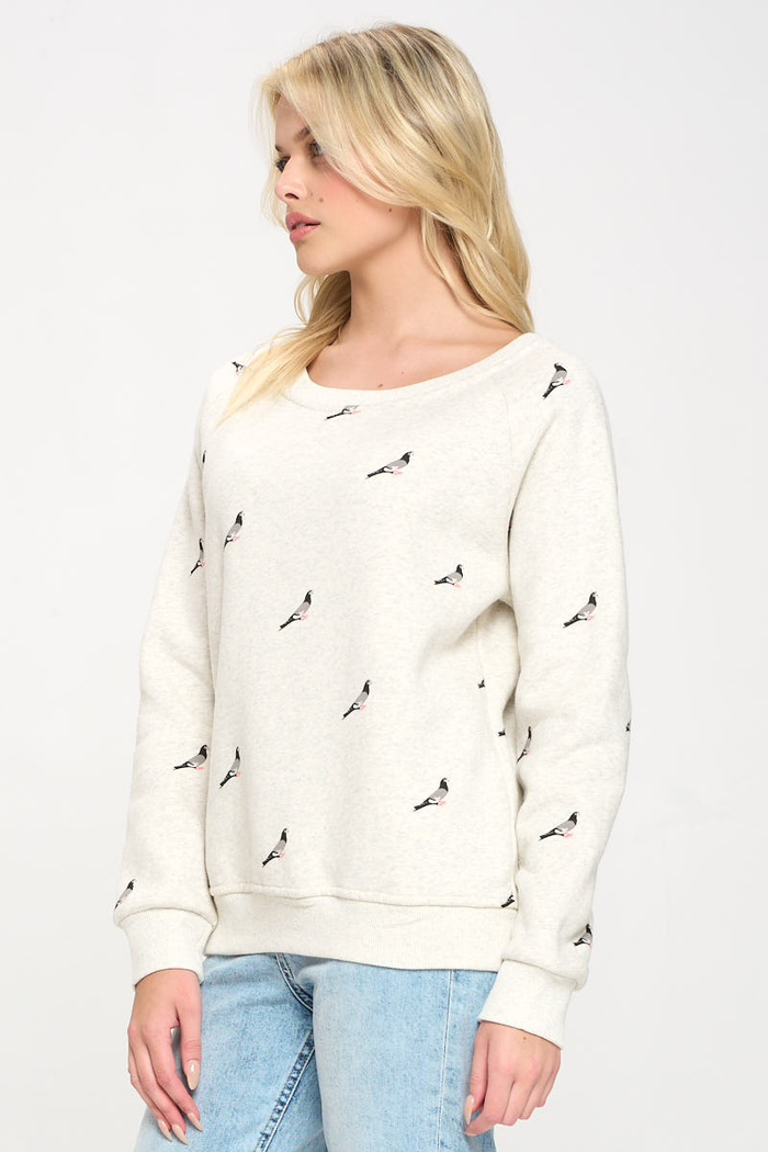 Image shows a woman wearing a crew neck heather gray sweatshirt with a pigeon print evenly repeated across the front, sleeves, and back, forming a continuous all‑over pattern rather than a single central graphic.