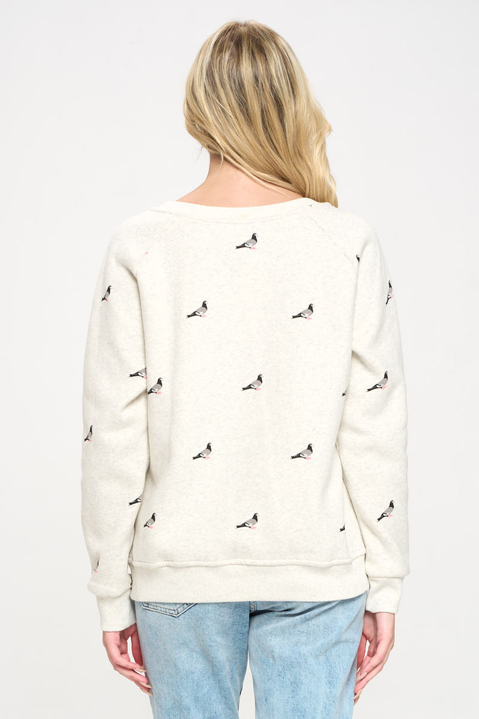 The image shows a rear view of a woman wearing a crew neck heather‑gray sweatshirt, featuring a pigeon print evenly repeated across the back and sleeves to create a continuous all‑over pattern.