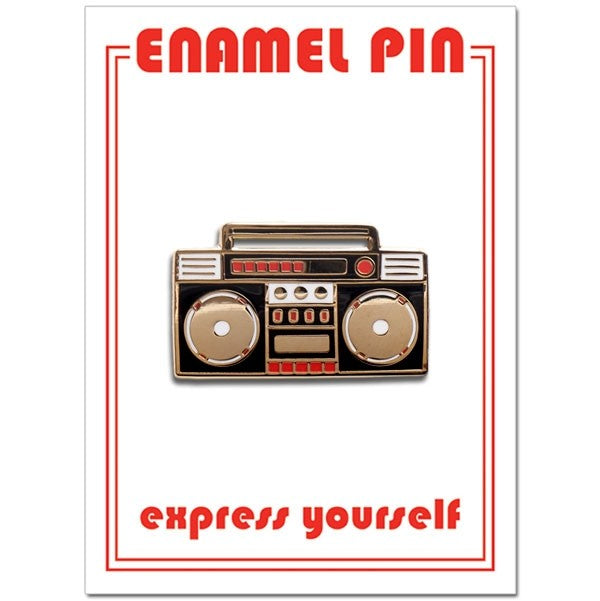 An enamel pin shaped like a 1980s boombox. It is primarily black with gold and red accents. Two large, round speakers sit on either side, with detailed cassette player buttons and controls in the center.