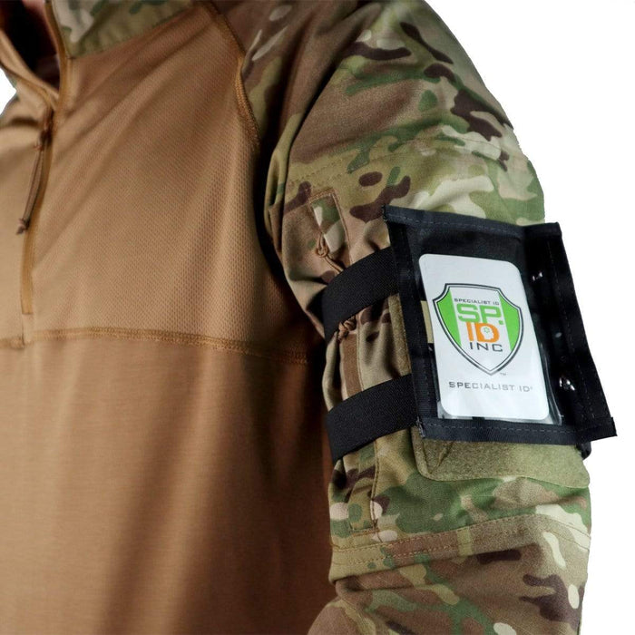 A person wearing a camouflage jacket with a Raine Military ID Badge Armband Holder with Two Straps (SPID-1090) displaying the logo "Specialist ID INC.