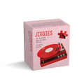 The box shows Jiggies in bright red whimsical lettering on a pink background, with the subtitle for when life gets too darn serious and a note that it’s a 50‑piece puzzle. The lower half displays a retro portable record player in red and black.