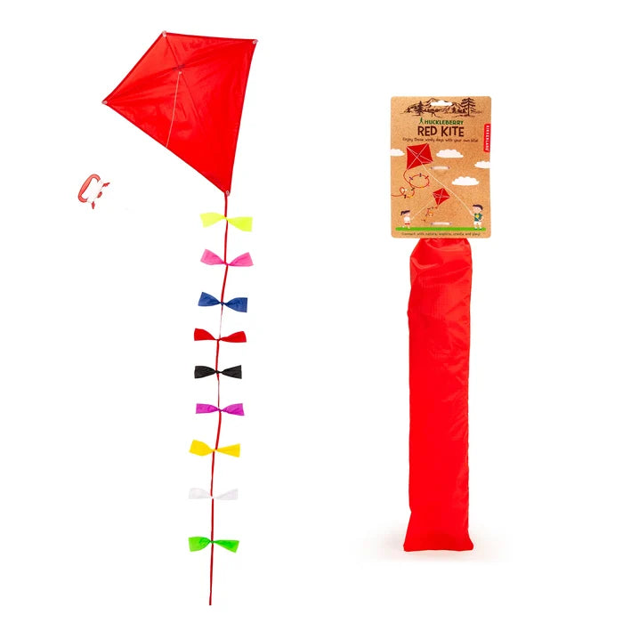 The image shows a classic, bright red diamond shaped kite with flowing multi color ribbon tails that add movement. The kite string is neatly looped around a matching red handle, and kraft card packaging.
