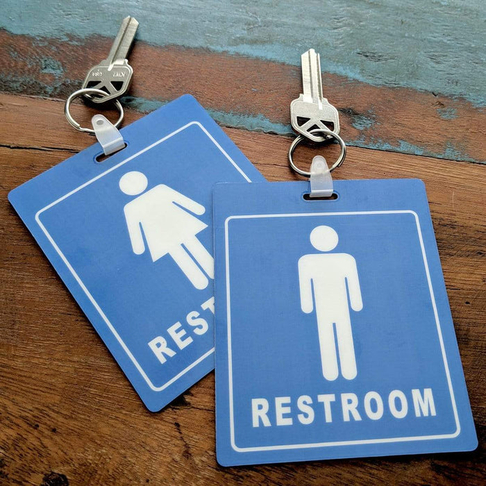 Two **Restroom Pass Keychain - Bathroom Tag with Key Chain Ring - Heavy Duty Large Passes for Men and Women Restrooms with Key Holder (Sold in 2 Pack) (SPID-9830-Blue)**, each with icons for male and female, are placed on a wooden surface.