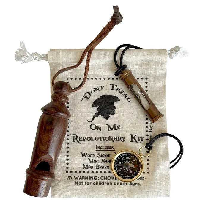 The image shows a Revolutionary War–themed kit on a white background. On top of a muslin drawstring bag printed with “Don’t Tread on Me” are a small wooden whistle, a 2‑inch brass sand timer necklace, and a gold‑colored compass with a black dial. The materials—wood, metal, and soft fabric—are easy to distinguish by touch.