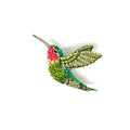 A close-up image shows a small, hand-embroidered brooch shaped like a hummingbird in mid-hover. Its body is slightly raised, giving it a soft, dimensional feel. The head and throat feature a vivid ruby-red patch that catches the light, while the rest of the bird shimmers in green tones with subtle neutral accents.The surface is richly textured, made from tightly stitched beads, sequins, and thread, creating a lifelike sparkle and a sense of delicate movement, as if the tiny bird has just paused in flight.