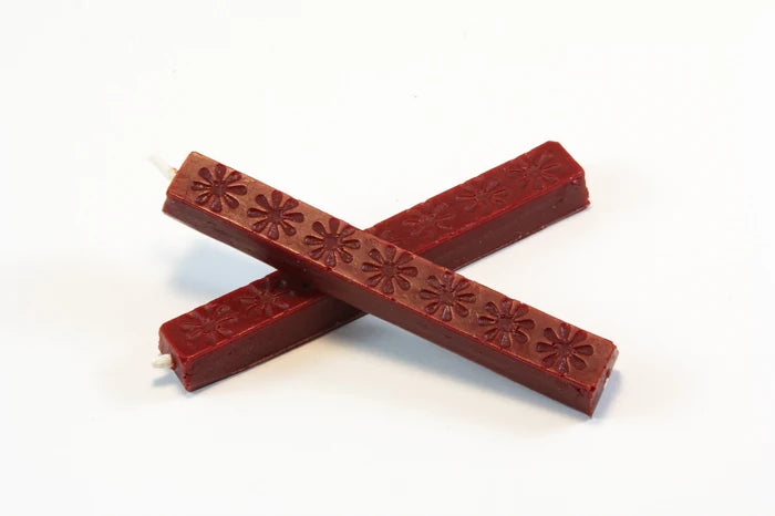 The image shows two 4‑inch burgundy wax sticks on a white background. The wax appears hard and smooth, with subtle daisy‑like embossed patterns. When melted, it becomes thick and pliable, then cools to a slightly flexible, buttery finish designed to resist cracking in the mail.