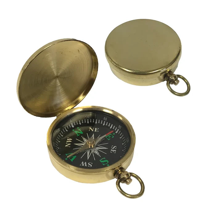 A small, round brass pocket compass shown on a white background. It has a smooth, polished case about 2 inches wide with a flip‑top hinged lid. Inside is a glass‑covered black compass face with raised white directional markings and a brass needle, plus a small side lever to lock the needle and a brass ring for attaching a chain. The image shows two views the compass open, and with the lid shut.