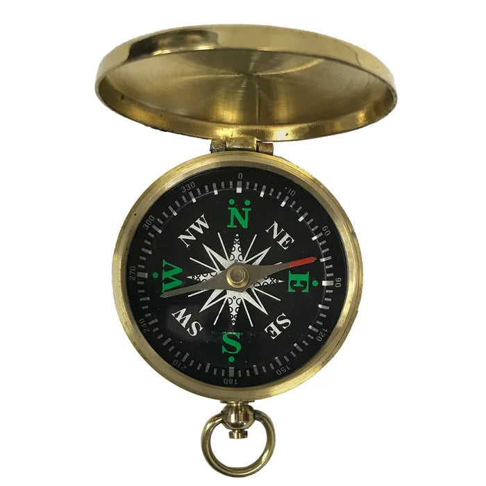 A small, round brass pocket compass shown on a white background. It has a smooth, polished case about 2 inches wide with a flip‑top hinged lid. The open compass reveals a glass‑covered black face with raised white directional markings, a brass needle, a small side lever to lock the needle, and a brass ring for attaching a chain.