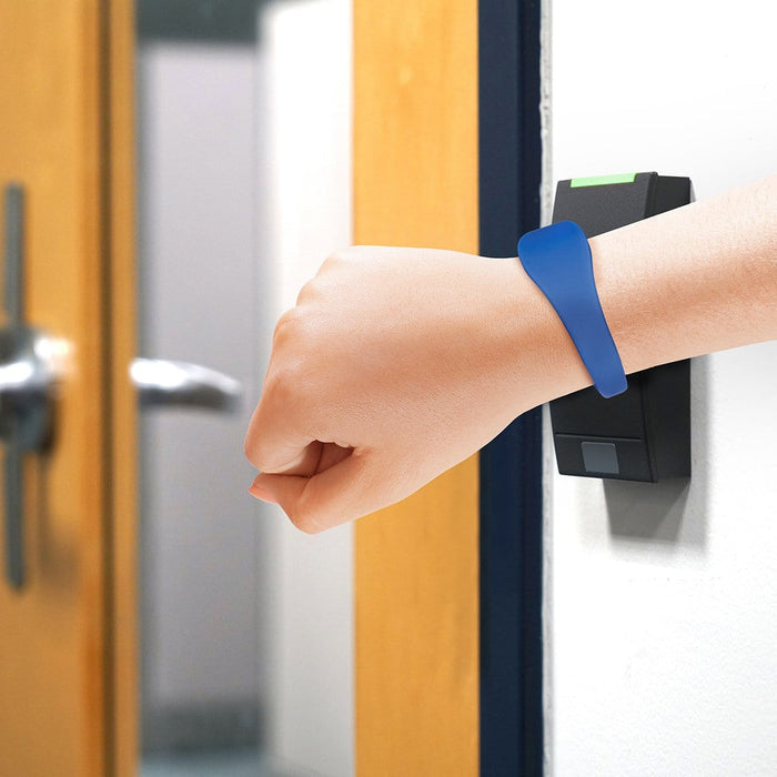 A person with a blue SPID UBand Proximity Silicone WristBand touches a black access control panel on a wall near a door handle. Sold by Specialist ID.