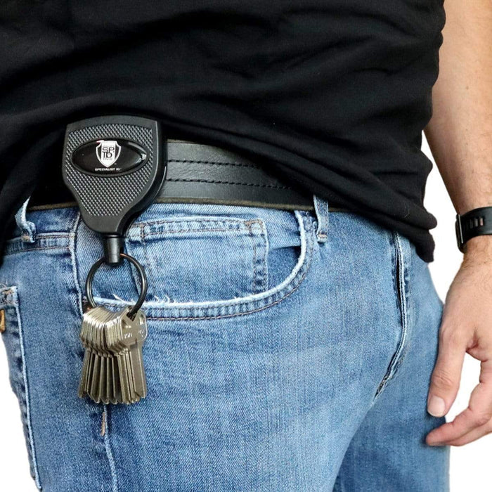 A person wearing blue jeans and a black shirt shows a set of keys attached to a Super Heavy Duty Retractable Keychain - 8oz or 10 Keys - Durable 48” (4 Ft) Kevlar Lanyard. Sold by Specialist ID.
