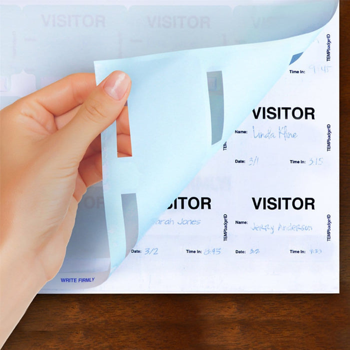 A hand flips a page in the Expiring Visitor Badge and Log Book - 480 Badges (05741), revealing visitor names including "Linda Hine," "Sarah Jones," and "Jeffrey Anderson" along with their sign-in dates and times, all meticulously recorded as part of the visitor management system.
