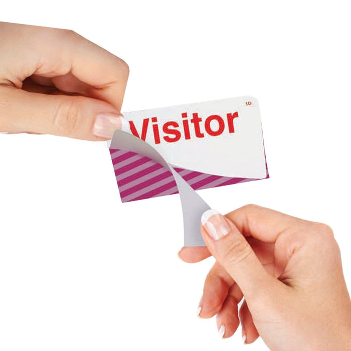 Two hands are peeling a sticker labeled "Visitor" off a striped card, demonstrating the use of One Step Manually-Issued Self-Expiring Badges, Box of 500 (P/N T200X) for visitor identification.
