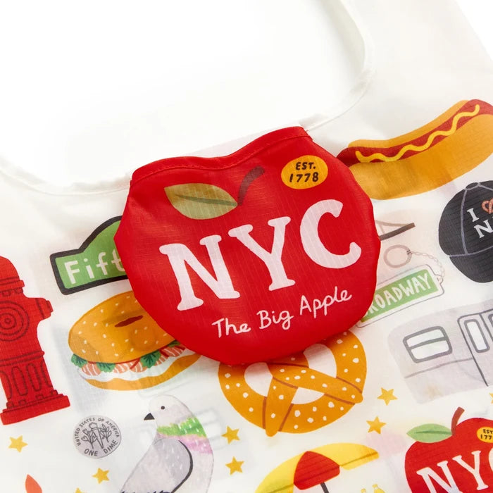 Integrated red apple-shaped pouch with 'NYC' and 'The Big Apple' text, attached to a white foldable carrier featuring a colorful print of bagels, pretzels, and Broadway signs.