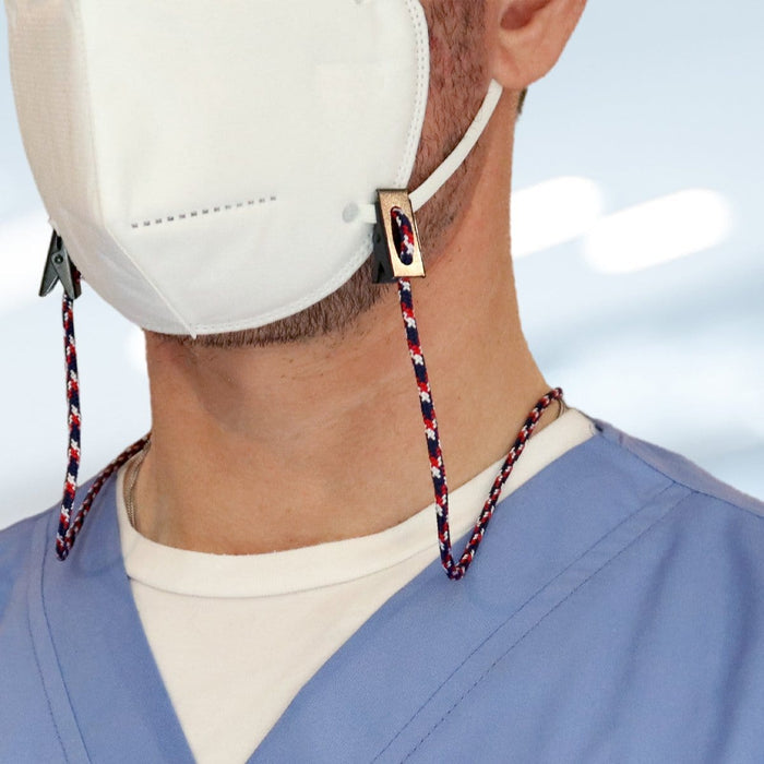 A person wearing a white face mask with a USA Made Adjustable Double Clip Lanyard - Woven Nylon Neck Hanger with 2 Bulldog Clips attached, dressed in light blue scrubs and a white undershirt.
