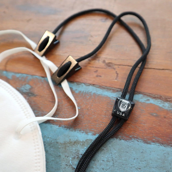 Close-up of a white face mask and a USA Made Adjustable Double Clip Lanyard - Woven Nylon Neck Hanger with 2 Bulldog Clips, featuring an "End of the Road" label and "USA" text, all placed on a wooden surface.