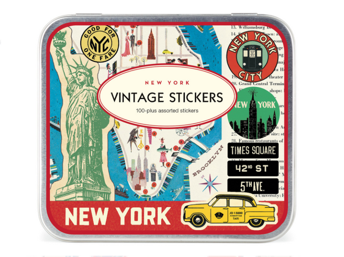 Overhead view of a small rectangular Cavallini & Co. keepsake tin with a hinged lid. The vintage-style design features a colorful collage in green, blue, cream, red and yellow, including the Statue of Liberty, a partial map of New York City, iconic landmarks, a yellow taxi, and classic city signs.