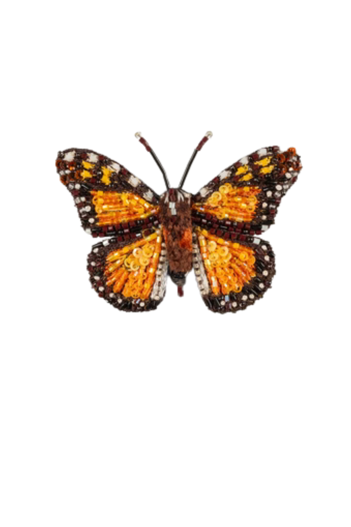 Wanderer Monarch Butterfly Brooch - A small butterfly brooch with outstretched wings, slightly wider than it is tall. The surface is layered with soft felt and detailed stitching, with raised beads and sequins that add texture and a light shimmer. The wings are patterned with structured lines and edges, giving a defined, symmetrical shape. A metal pin on the back allows it to be fastened to clothing. Each handmade piece varies slightly in detail and texture.