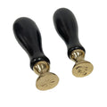 Two antique‑style wax seal stamps—a fleur‑de‑lis and a leaf—shown on a white background. Each has a dark cherry‑stained wooden handle and a 1⅛‑inch round solid brass seal with a distressed finish. The seals are about 5½ inches tall, interchangeable, and designed for use with traditional hard sealing wax. Sold separately.